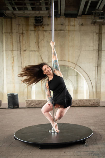 Caucasian middle aged female pole dancer outside White female pole dancer on a stage pole outdoor under a highway overpass with arched supports and lots of concrete. black pole dancers stock pictures, royalty-free photos & images