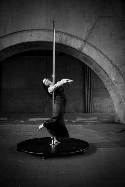 Caucasian middle aged female pole dancer outside White female pole dancer on a stage pole outdoor under a highway overpass with arched supports and lots of concrete. black pole dancers stock pictures, royalty-free photos & images