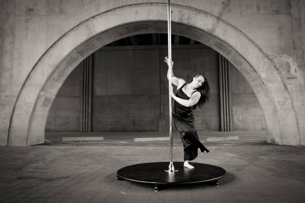 Caucasian middle aged female pole dancer outside White female pole dancer on a stage pole outdoor under a highway overpass with arched supports and lots of concrete. black pole dancers stock pictures, royalty-free photos & images