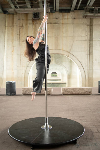 Caucasian middle aged female pole dancer outside White female pole dancer on a stage pole outdoor under a highway overpass with arched supports and lots of concrete. black pole dancers stock pictures, royalty-free photos & images