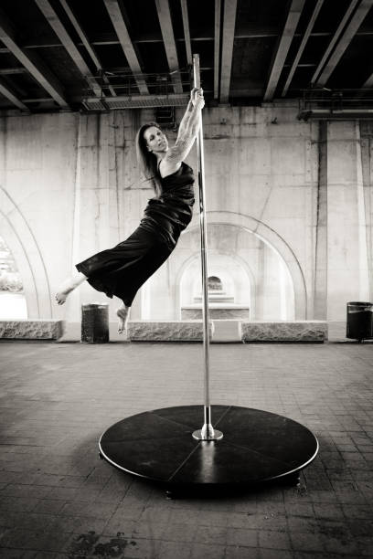 Caucasian middle aged female pole dancer outside White female pole dancer on a stage pole outdoor under a highway overpass with arched supports and lots of concrete. black pole dancers stock pictures, royalty-free photos & images