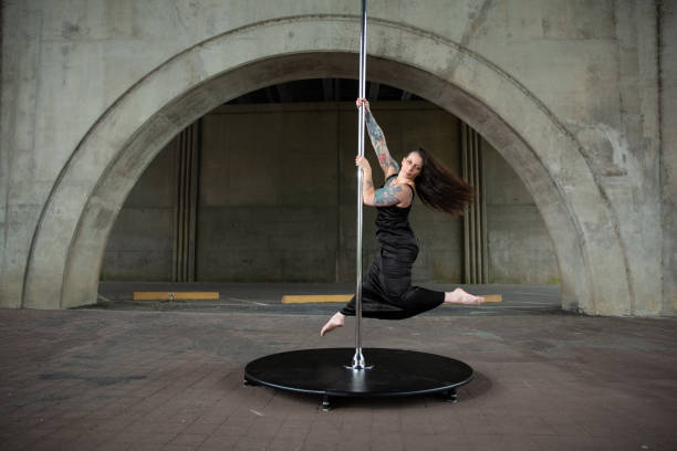Caucasian middle aged female pole dancer outside White female pole dancer on a stage pole outdoor under a highway overpass with arched supports and lots of concrete. black pole dancers stock pictures, royalty-free photos & images