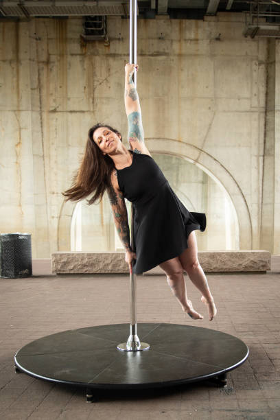 Caucasian middle aged female pole dancer outside White female pole dancer on a stage pole outdoor under a highway overpass with arched supports and lots of concrete. black pole dancers stock pictures, royalty-free photos & images