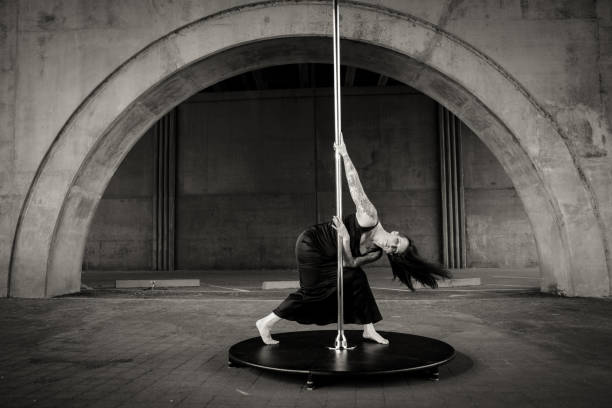 Caucasian middle aged female pole dancer outside White female pole dancer on a stage pole outdoor under a highway overpass with arched supports and lots of concrete. black pole dancers stock pictures, royalty-free photos & images