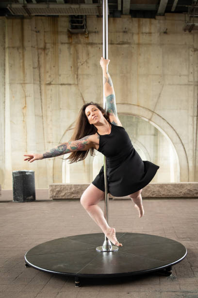 Caucasian middle aged female pole dancer outside White female pole dancer on a stage pole outdoor under a highway overpass with arched supports and lots of concrete. black pole dancers stock pictures, royalty-free photos & images