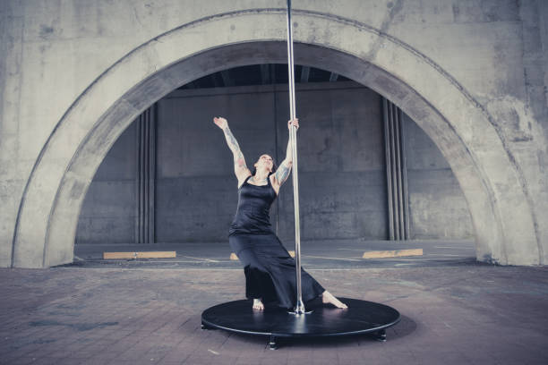 Caucasian middle aged female pole dancer outside White female pole dancer on a stage pole outdoor under a highway overpass with arched supports and lots of concrete. black pole dancers stock pictures, royalty-free photos & images