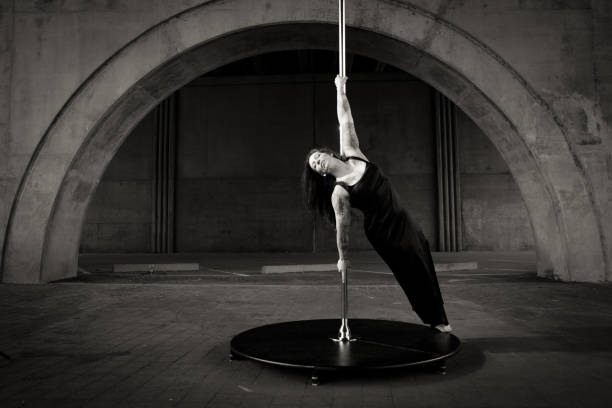 Caucasian middle aged female pole dancer outside White female pole dancer on a stage pole outdoor under a highway overpass with arched supports and lots of concrete. black pole dancers stock pictures, royalty-free photos & images