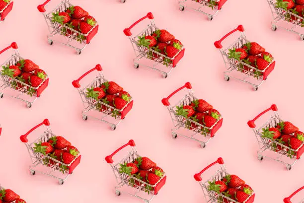 Pattern of fresh red strawberry in shopping cart on pink background. Online shopping and Valentines Day minimalistic concept. Black Fridays sales banner. Healthy, organic, vegan food