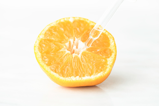 Front view of pipette with serum above sliced orange fruit  on pure white background.
