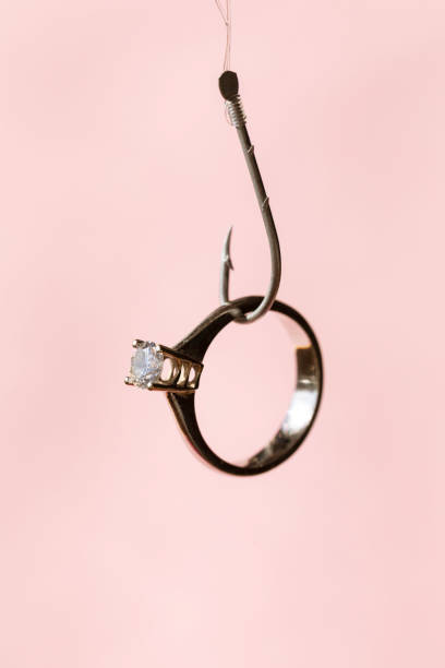 Solitaire diamond ring hanging at fishing hook . Representing online dating apps and phishing concepts.
