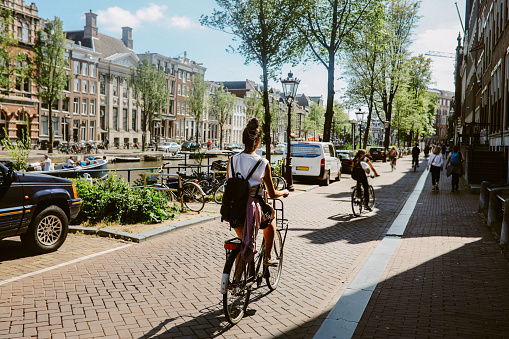 Woman cycling in Amsterdam, commuting or just sightseeing on a bright summer day.