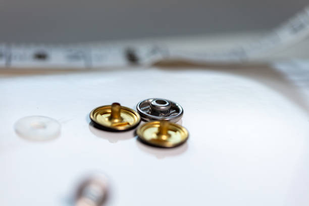 Gold press-studs with a small button with a tape measure in the background. The background is grey in colour.