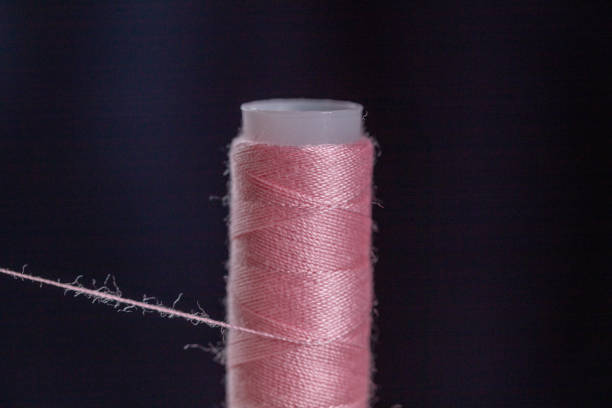 A cotton reel with pink cotton wrapped around it, with a black background. A cotton reel with pink cotton wrapped around it, with a black background.