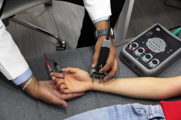 Photo of doctor's hands conducting electromyography study and nerve conduction in young woman