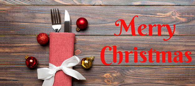 Merry Christmas text. Top view Banner of holiday set of fork and knife on wooden background. Christmas decorations and toys with copy space. New Year Eve concept.