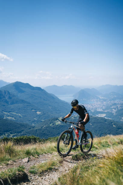 Athlete rides e-mountain bike on trail above mountains stock photo