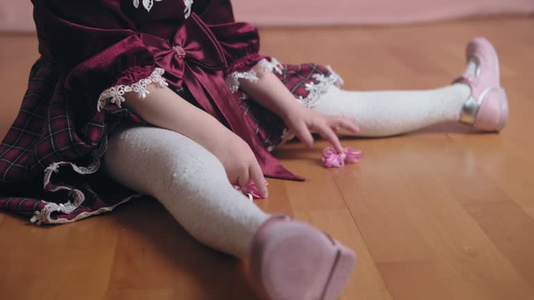 Cute little girl in vintage burgundy dress is playing with hair clip. Close up