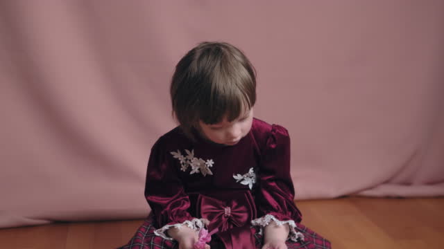 Cute little girl in an vintage burgundy dress is playing with a hair clip