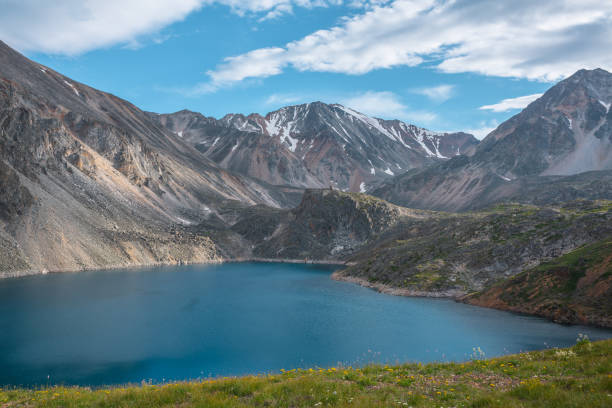 istock Deep mountain lake of phantom blue color among sharp rocks and high mountains in changeable weather. Wonderful dramatic view from sunlit grassy hill to deep blue alpine lake and rocks under cloudy sky 1416088695