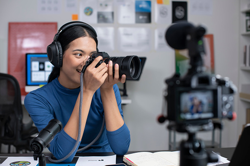 Young Asian female graphic designer blogger influencer filming teaching camera tutorial while looking at camera shooting education tutorial vlog training filming video course for social media at studio.