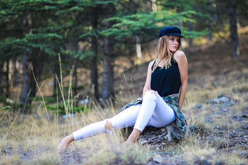 Young blonde woman in a hat posing among pine trees . fashion shoot