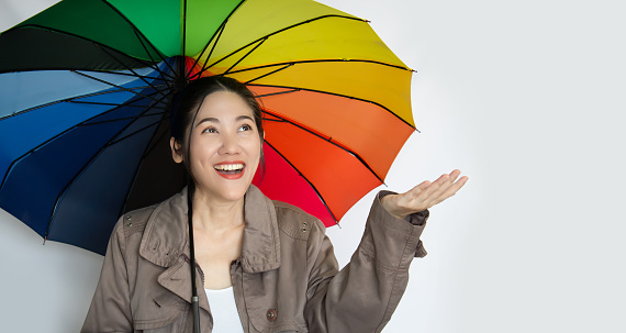 Asian beautiful  woman holding colorful umbrella looking up to see raining with smile and happiness