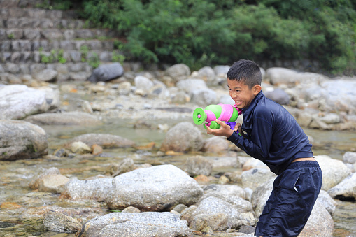 Japanese junior high school student playing in the river with water gun (12 years old boy)