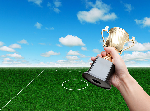 Hand holding golden trophy cup in soccer field