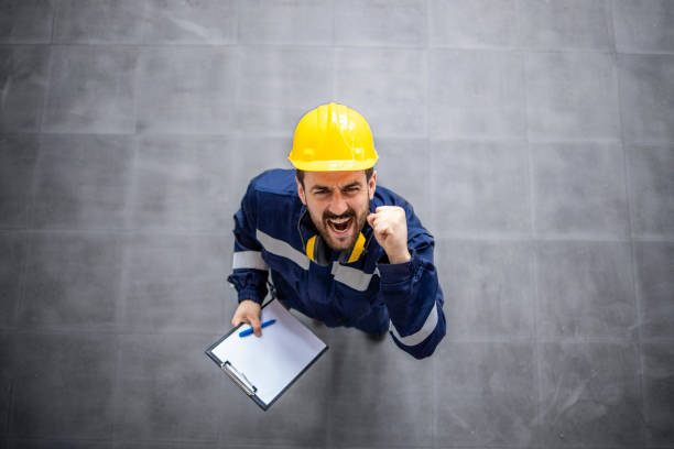 Top view of happy factory worker in protective work wear and hardhat celebrating job results, promotion and success. stock photo