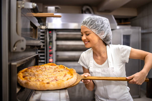 Pizza master taking freshly baked crunchy pizza from the oven in bakery.