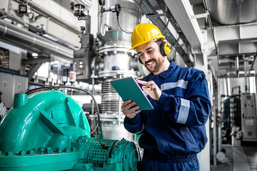 Professional petrochemical worker checking gas generator in power plant or refinery.