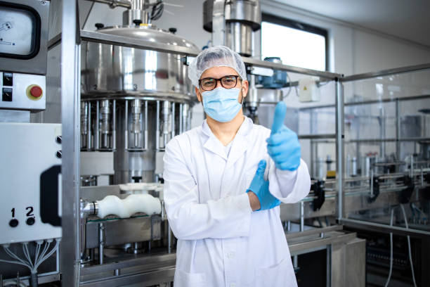 portrait of technologist or worker in sterile white clothing standing by automated industrial machine in pharmaceutical company or factory. - farmaceutische fabriek stockfoto's en -beelden