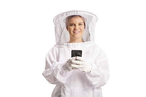 Young female bee keeper in a uniform holding a smartphone and looking at camera isolated on blue background