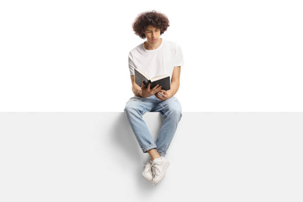 jovem com cabelo encaracolado sentado em um painel e lendo um livro - men reading outdoors book - fotografias e filmes do acervo
