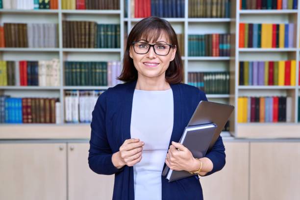 porträt einer lehrerin mit laptop in der hand in der bibliothek - professor librarian university library stock-fotos und bilder