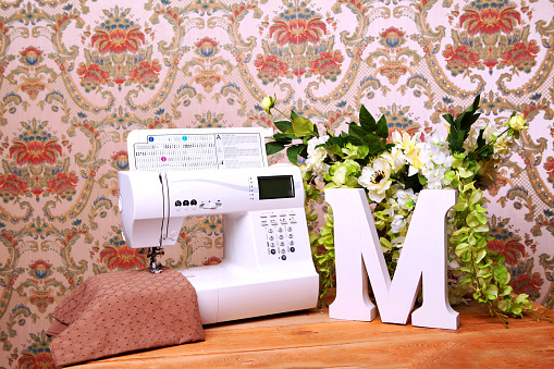 Composition from a sewing machine. Mannequin, flowers on a retro table and threads. Sewing supplies and composition with a sewing machine in the interior. With the letter M. The composition is unique for the fashion.