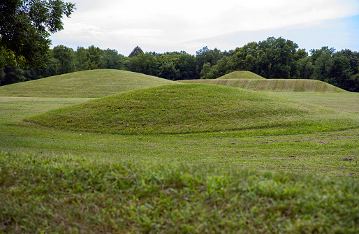 Native American Hopewell Culture prehistoric Earthworks burial mounds in Mound City park Ohio. Ancient circular mounds and long mound in the background. Grass is neatly trimmed with trees and dramatic sky.