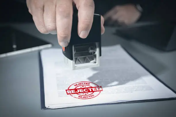 Close-up Of Person Hand Stamping With Rejected Stamp On Text denied Document At Desk, Contract Form Paper. Businessman signing business project rejection stamp