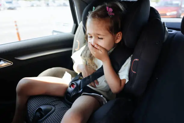 Five years old small child in the backseat of a car sitting in children safety car seat covers his mouth with his hand -