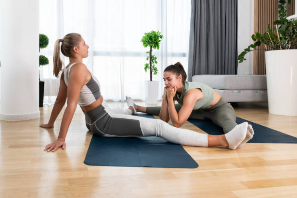 Two young colleagues, roommates, friends or lesbian couple workout yoga together stretching muscles in their apartment as relaxing breathing exercise for happy and healthy life. Two young colleagues, roommates, friends or lesbian couple workout yoga together stretching muscles in their apartment as relaxing breathing exercise for happy and healthy life. real wife stories stock pictures, royalty-free photos & images