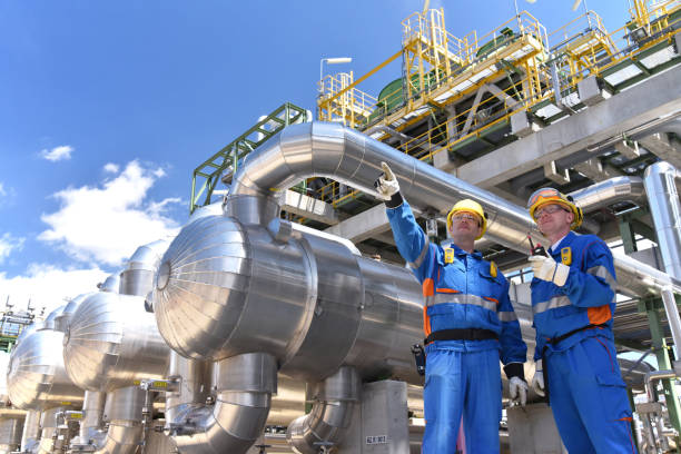 trabajo en equipo: grupo de trabajadores industriales en una refinería - equipos de procesamiento de petróleo y maquinaria - industria petrolera fotografías e imágenes de stock