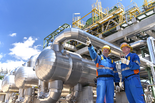 teamwork: group of industrial workers in a refinery - oil processing equipment and machinery
