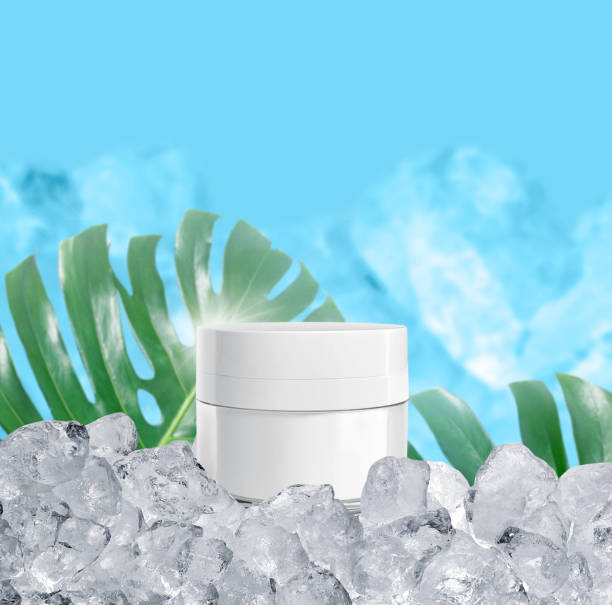 istock Whitening cream in a glistening white spherical base packaging with ice cubes on blue background and tropical plants, for cosmetic advertisements 1416380405
