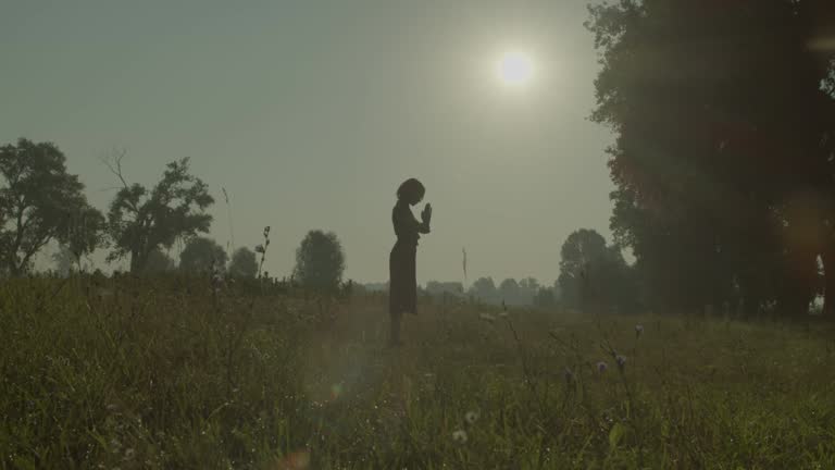 Faithful attractive female saying prayers to god in summer nature at dawn