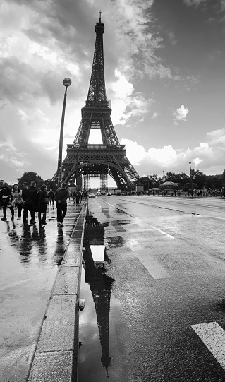 black and white shot of the bridge Pont d'Iéna, with a view of the Eiffel Tower, the famous landmark of the city of Paris. wet street covered with puddles in which the Eiffel Tower is reflected. 06/05/2022 - Pont d'Iéna, 75116 Paris, France
