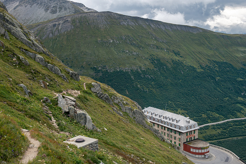 View from a mountain hiking trail above the Furka Pass of the building and the mountains surrounding the pass road. Destination for trips to the Alps or to the nearby Rhone glacier and for nature lovers, hikers, climbers or motorcyclists and cyclists. 08/28/2021 - Belvédère, 3999 Obergoms Wallis, Switzerland