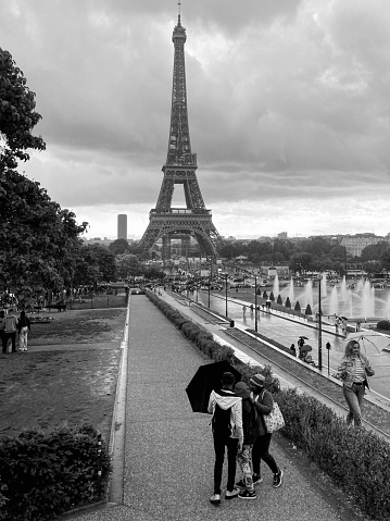 Tourist with umbrellas and raincoats look to the landmark of Paris, the Eiffel Tower under a heavy cloudy sky. 06/05/2022 -1 Av. Gustave V de Suède, 75116 Paris, France