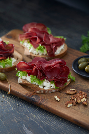 Sandwiches with smoked ham, cheese and  lettuce, brunch serving suggestions, served on a dark wooden cutting board, and dark mood table