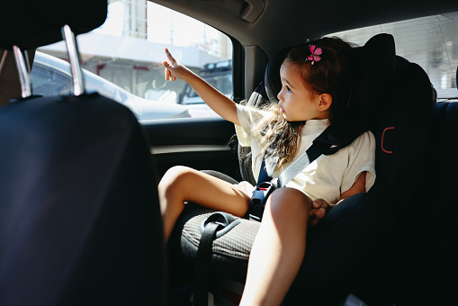 Cheerful smiling girl sitting in car safety seat and having fun.