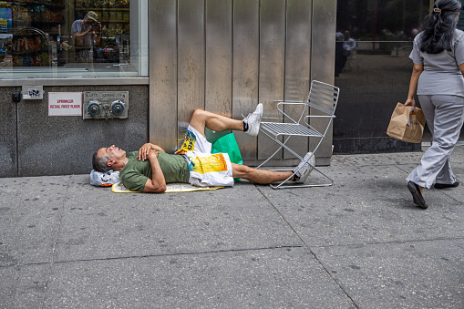 Manhattan, New York, NY, USA - July 8th 2022: Homeless man sleeping on the sidewalk in Times Square in a early afternoon